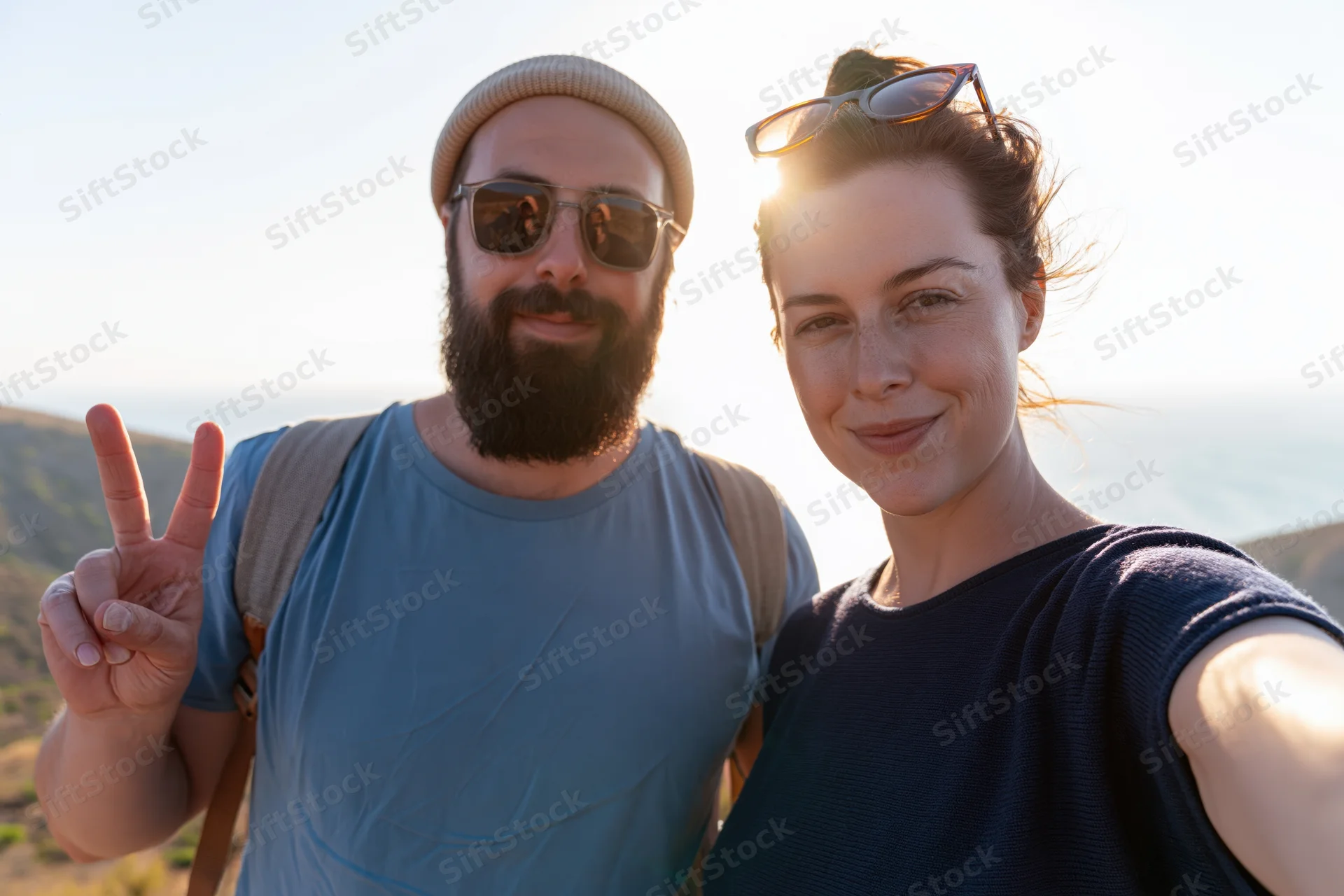 Couple taking selfie outdoors with backpack and sunglasses near beach and mountains