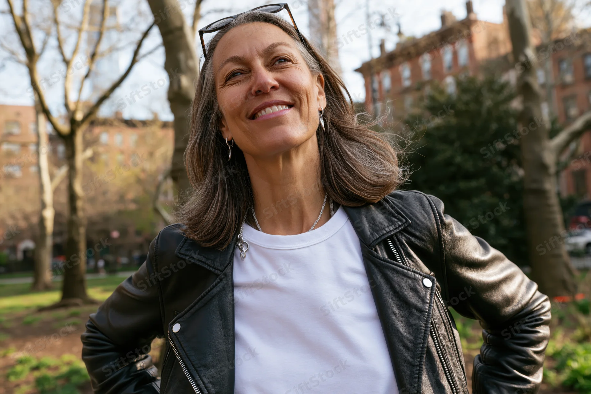 Middle-aged woman smiling outdoors in a park wearing a leather jacket and white t-shirt