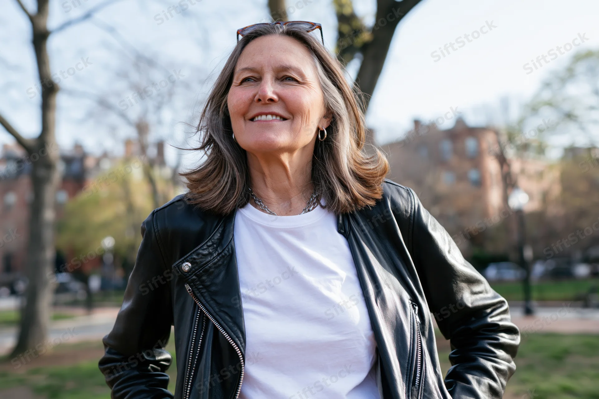 Middle-aged woman smiling outdoors in a park wearing a leather jacket and white t-shirt