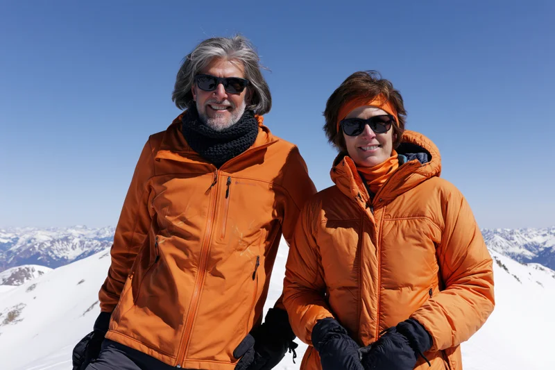 Couple in orange jackets smiling on snowy mountain ridge