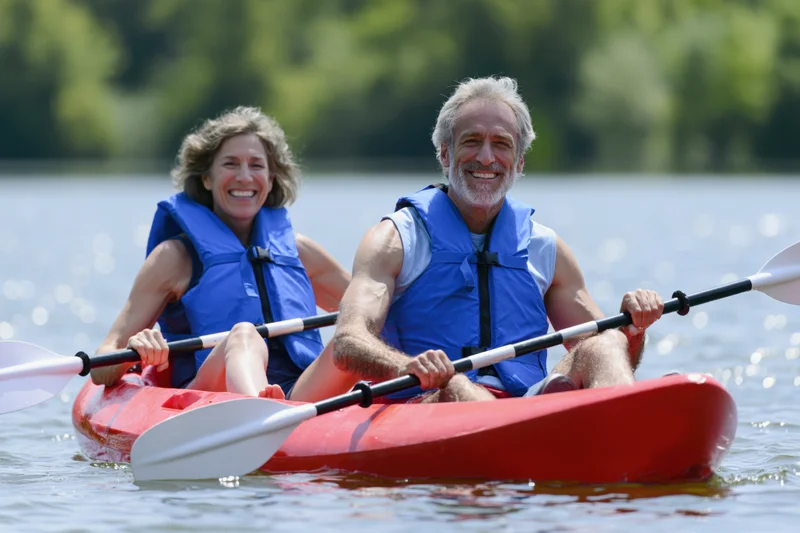Senior couple paddling in a red tandem kayak on calm water