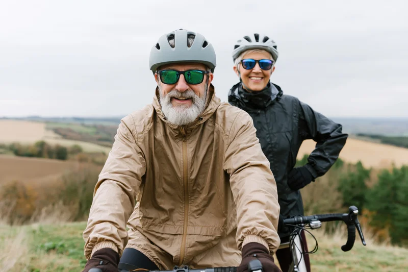 Senior man and woman cyclists smiling on a rural trail with bicycles, outdoors in autumn countryside