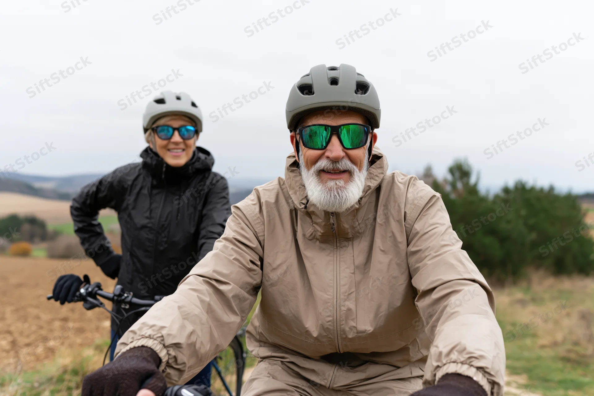 Senior man and woman cyclists smiling while riding bikes in a rural field