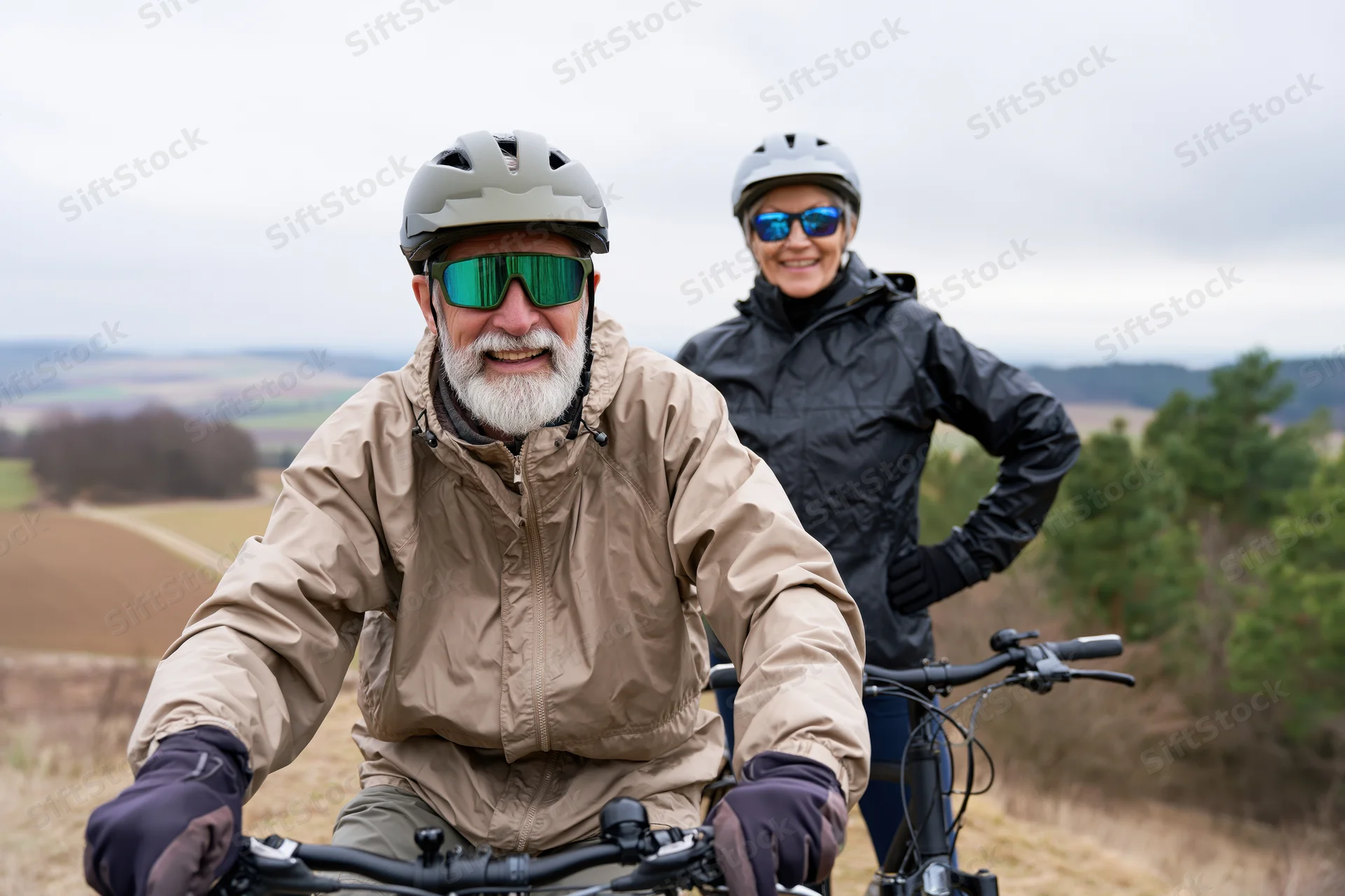 Senior man and woman cyclists posing outdoors on a rural trail with bicycles and protective gear