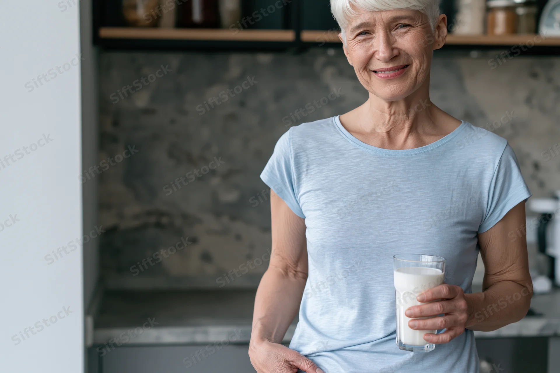 Senior woman smiling while holding a glass of milk in a modern kitchen