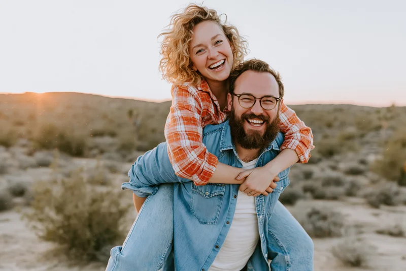 Man giving woman a piggyback ride in desert at sunset