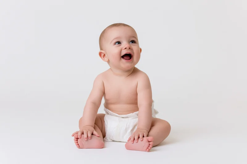 Baby sitting on white seamless backdrop smiling with mouth open