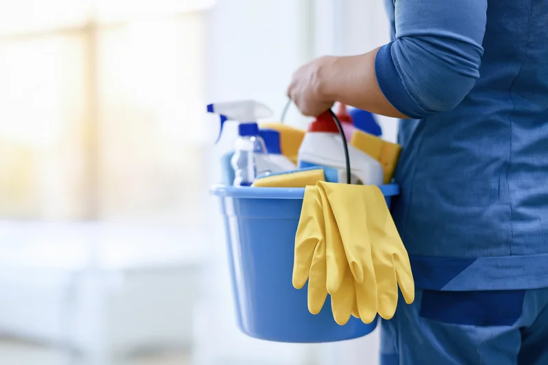Woman carrying a blue bucket filled with cleaning supplies indoors