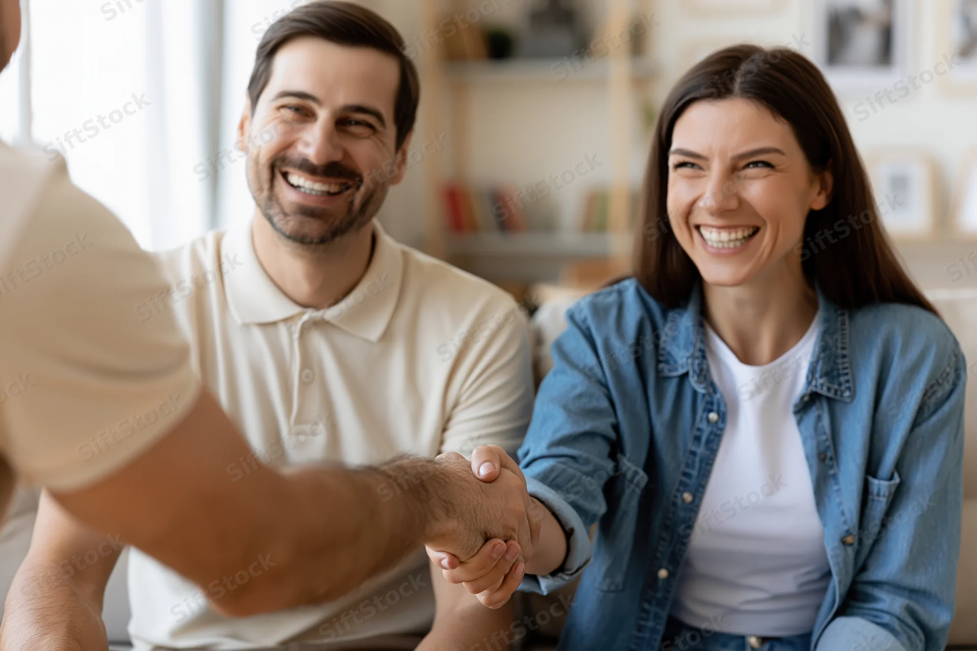 Man and woman sitting on sofa shaking hands with someone smiling