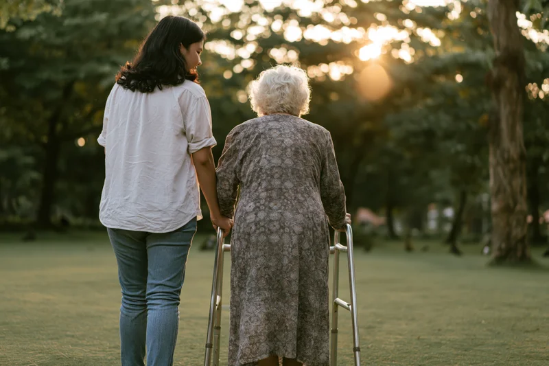 Young asian woman supporting elderly asian woman with walker in park at sunset