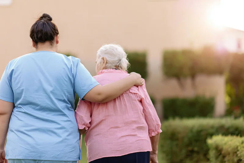 Caregiver walking arm-in-arm with senior woman in garden at sunset