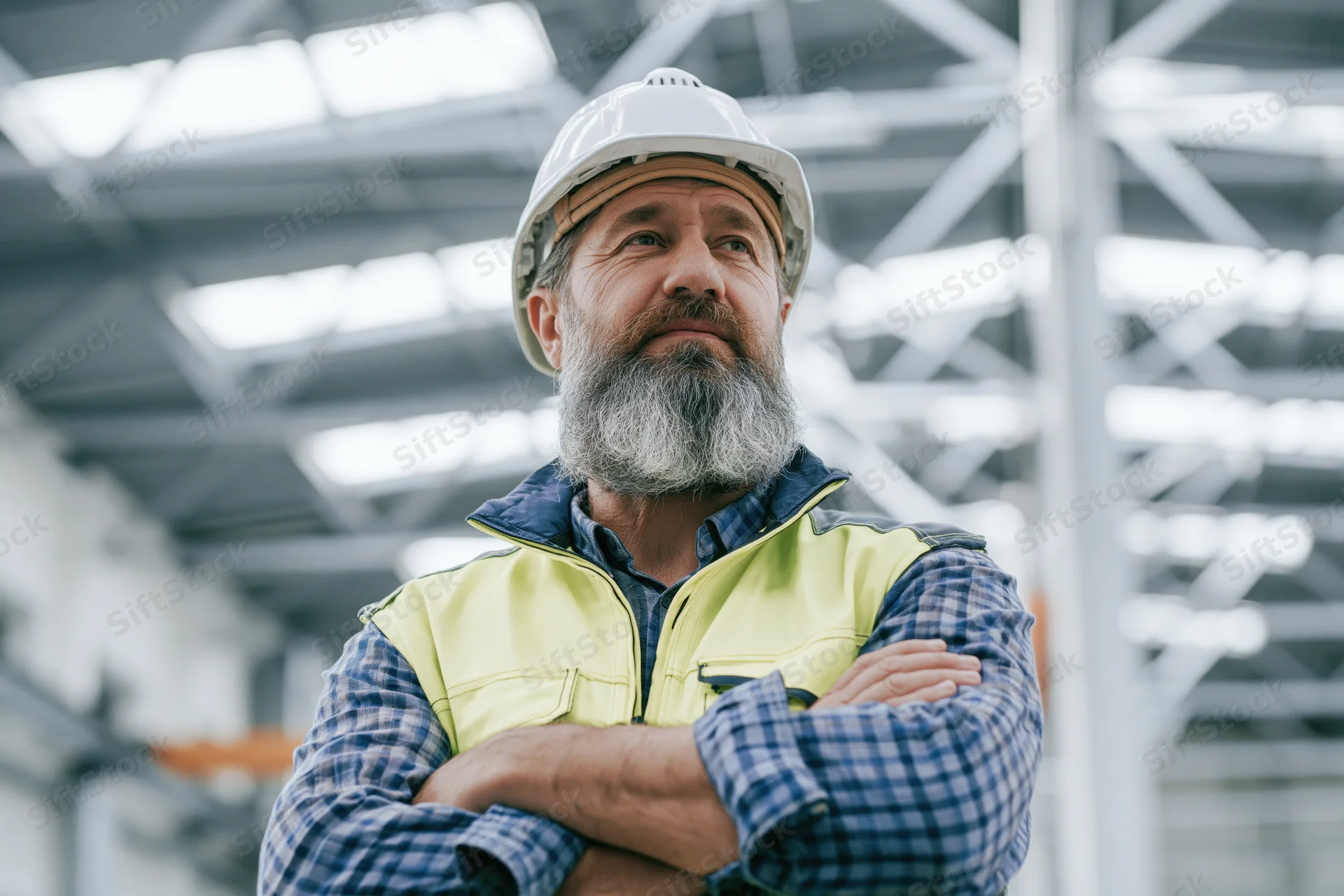 Bearded male engineer in his fifties standing with arms crossed in a factory setting