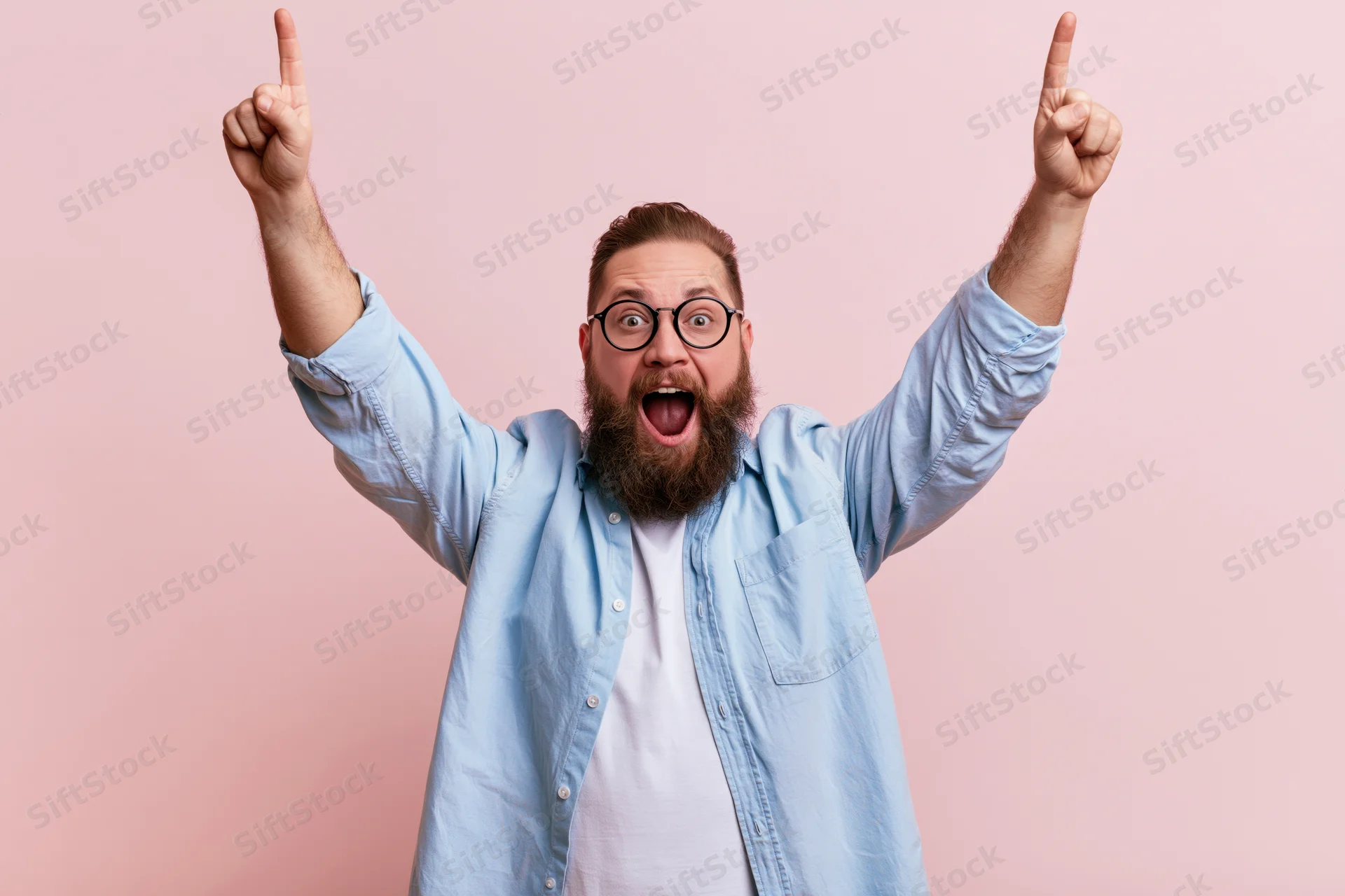 Bearded man celebrating with arms raised pointing upward against pink background