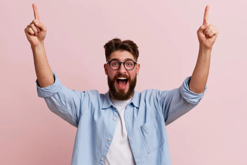 Bearded man celebrating with arms raised pointing upward against pink background