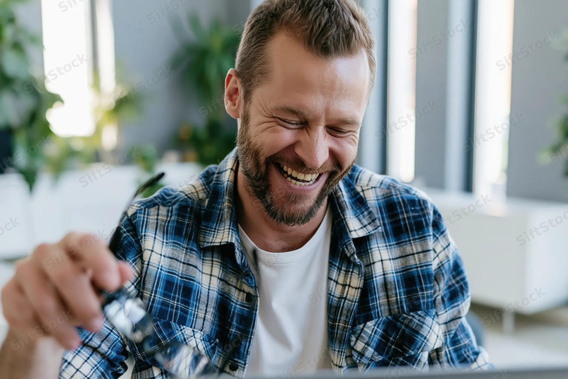 Bearded man laughing while looking at laptop in modern office space