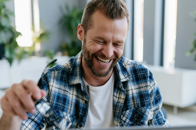 Bearded man laughing while looking at laptop in modern office space