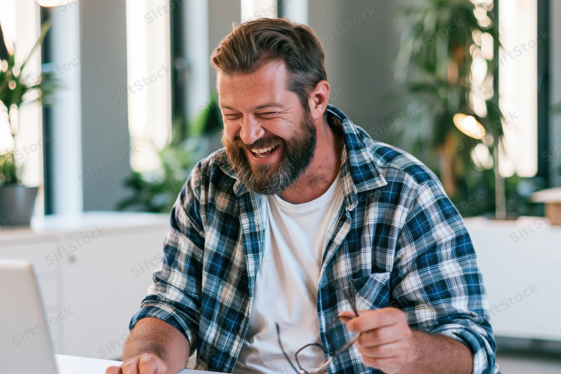 Bearded man laughing while using laptop at home office desk