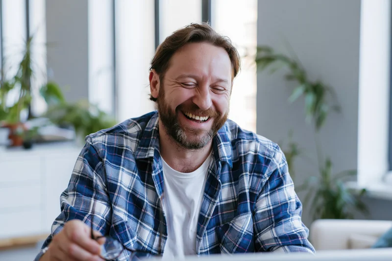 Bearded man laughing while looking at laptop in modern home office