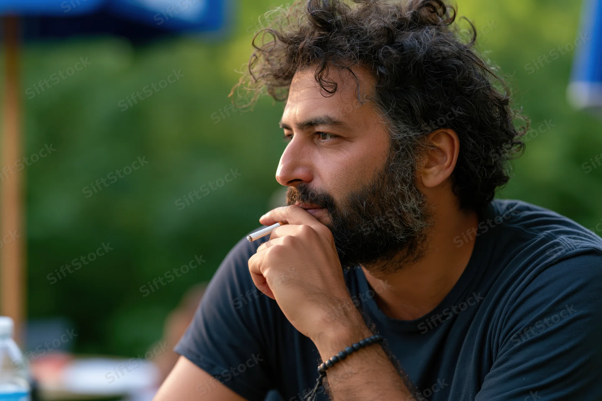 Bearded man smoking a cigarette in profile outdoors at a patio table