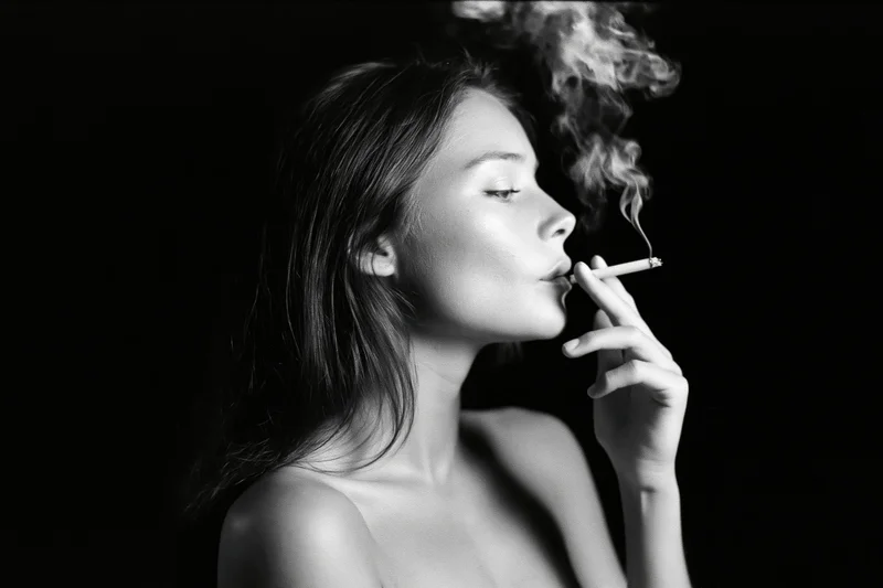Young woman in profile exhaling smoke from a cigarette against a dark background