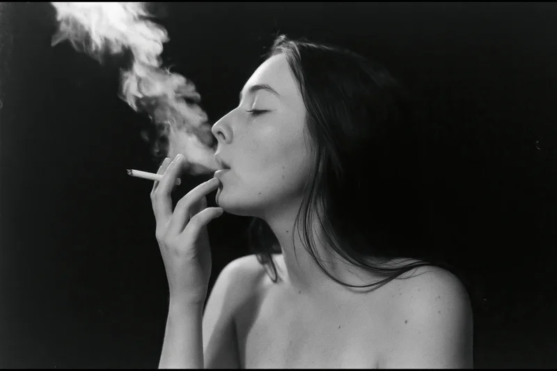 Young woman in profile exhaling smoke from a cigarette against dark background