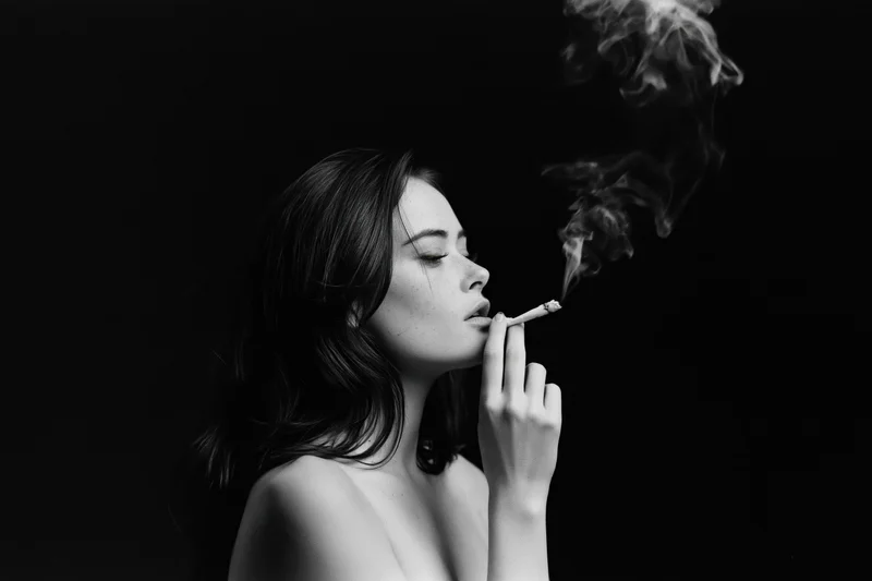 Young woman in profile smoking a cigarette against dark background
