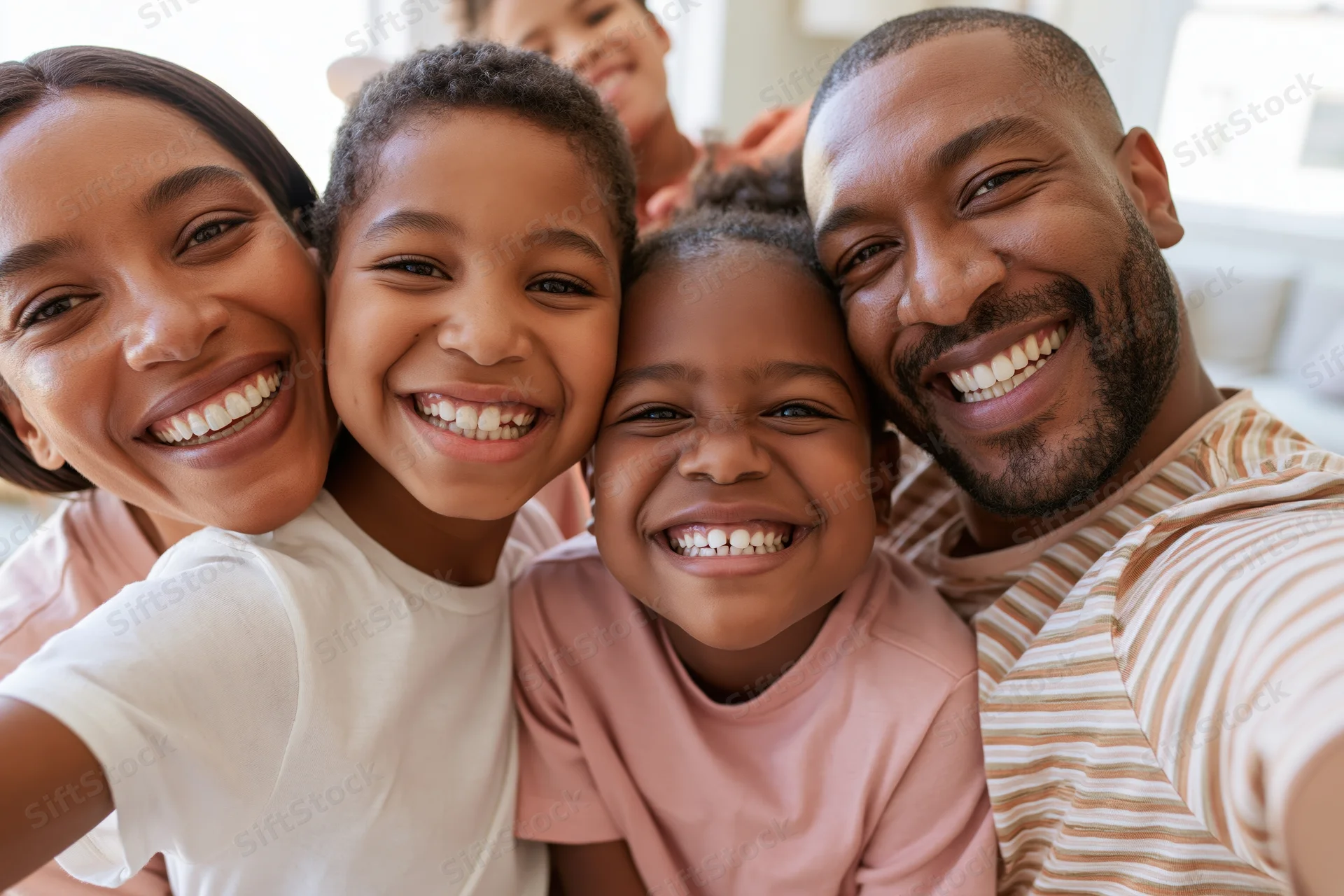 Black family of four smiling closely together in a home setting taking a selfie