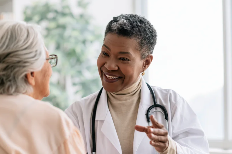 Black female doctor smiling while talking with an elderly patient in a clinic
