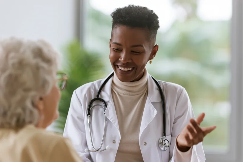 Black female doctor smiling while talking with an elderly patient in a clinic office