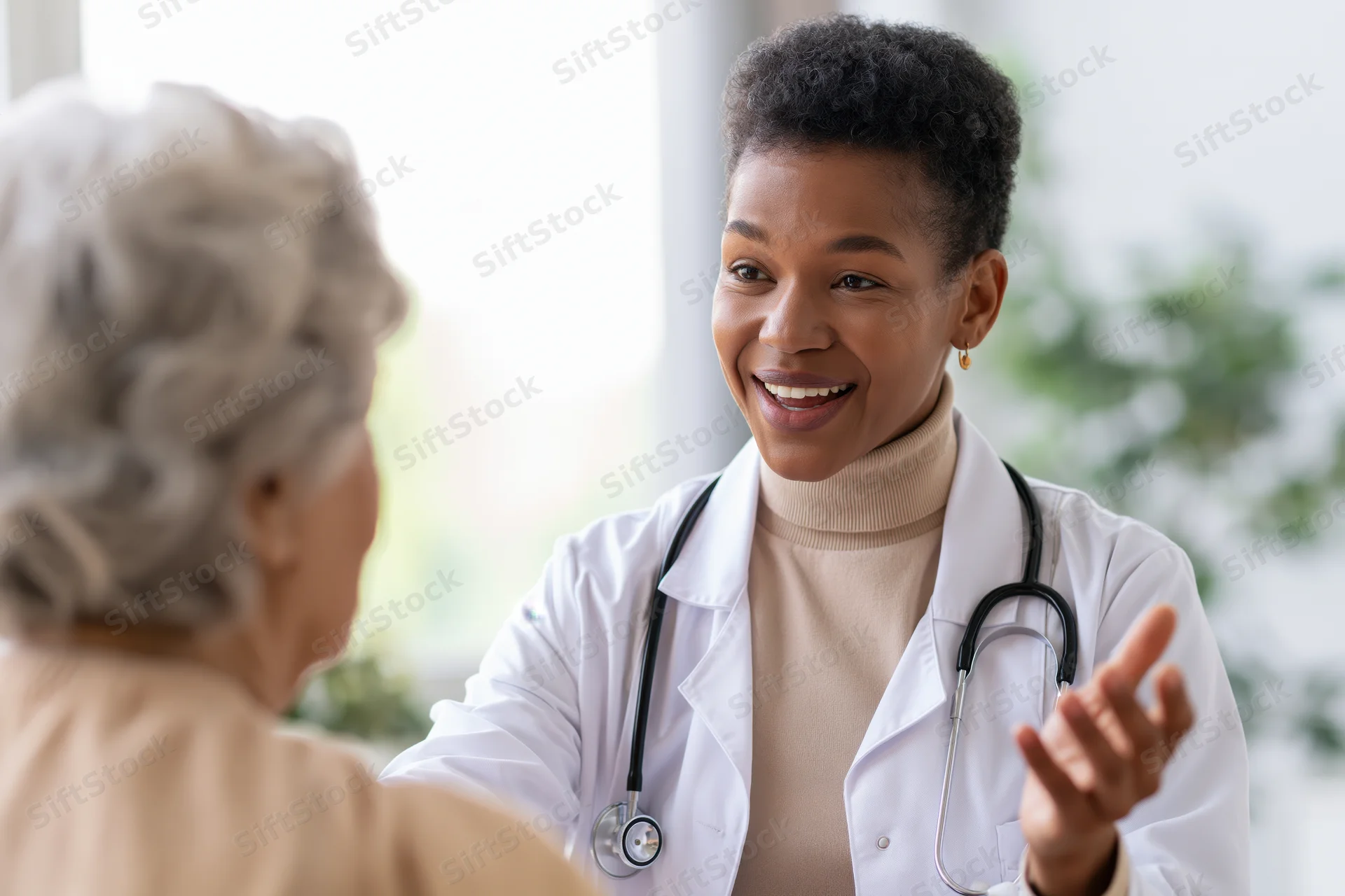 Black female doctor smiling while talking with senior patient in clinic office