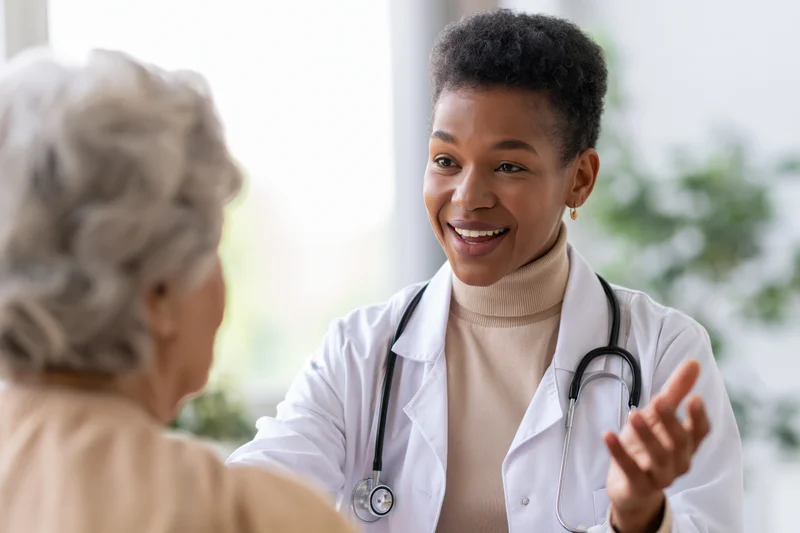 Black female doctor smiling while talking with senior patient in clinic office