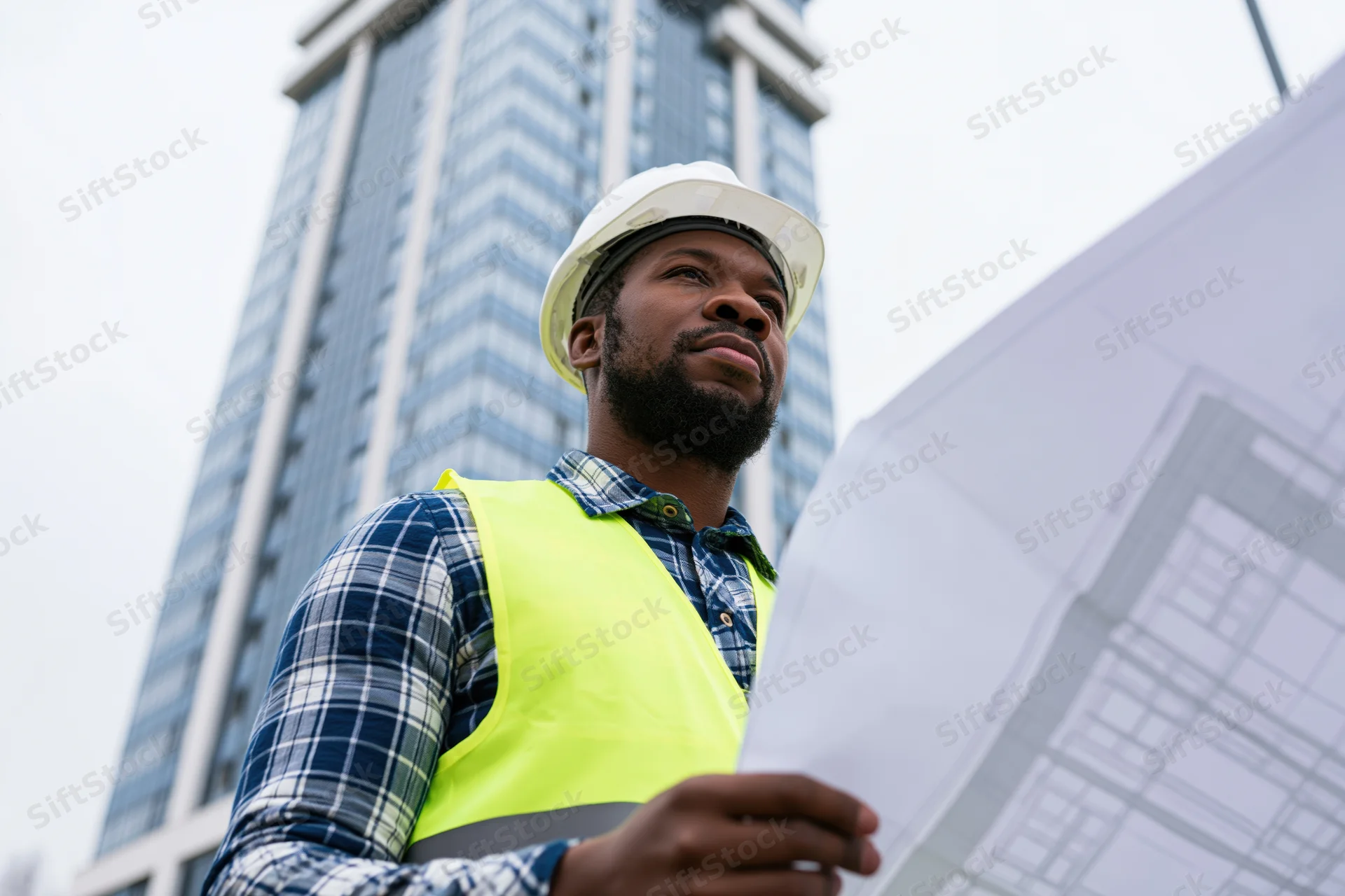Black male construction engineer reviewing blueprint on urban building site