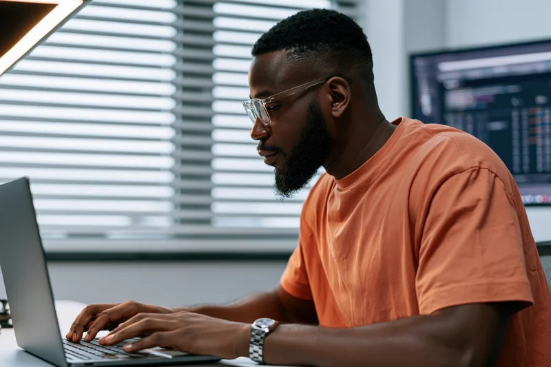 Black man typing on laptop at desk in office workspace