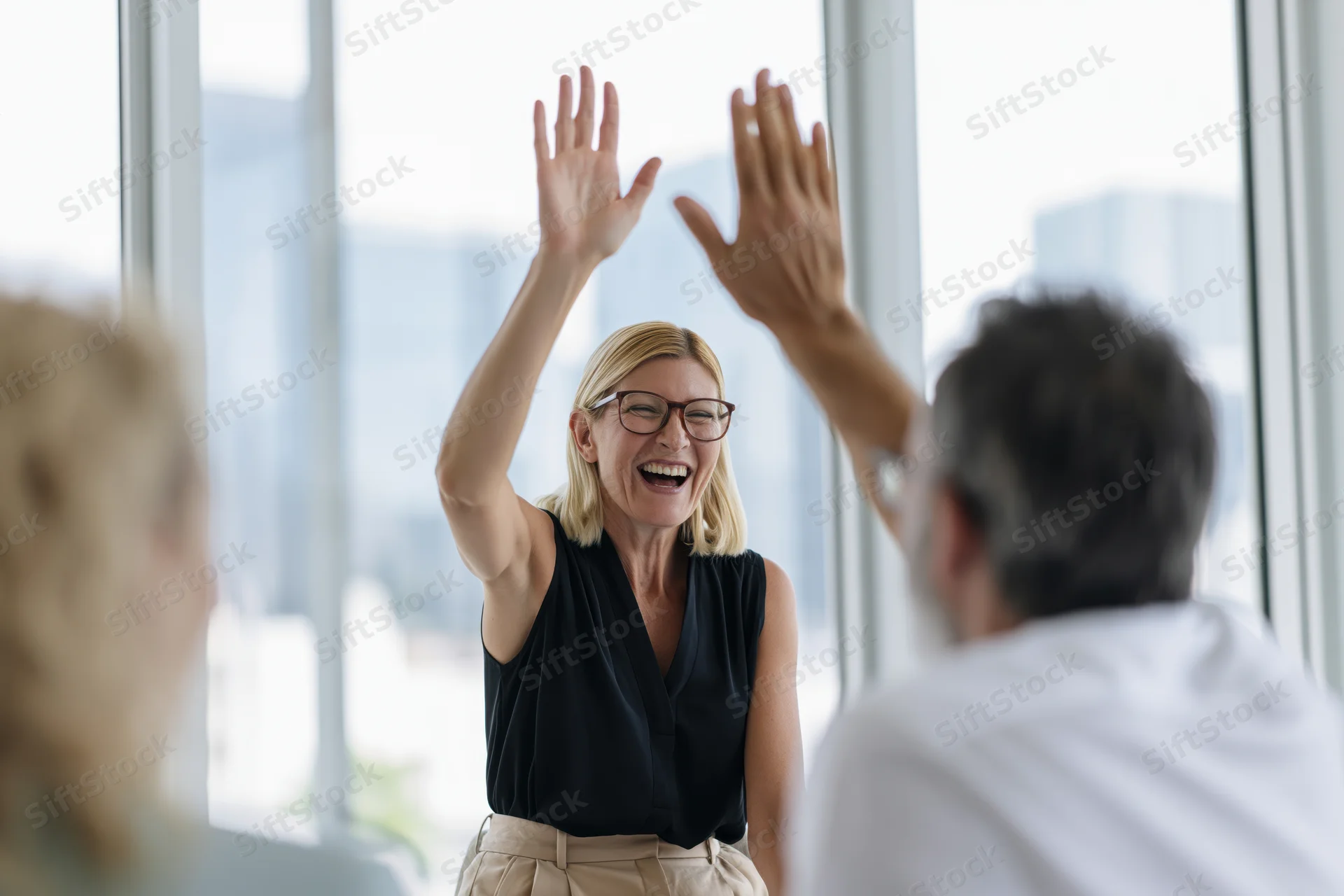 Woman laughing and high-fiving a colleague in an office meeting