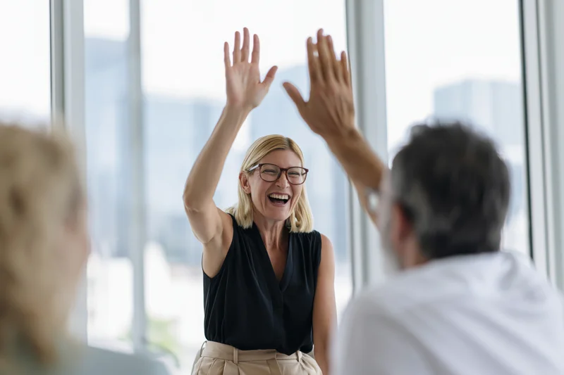 Woman laughing and high-fiving a colleague in an office meeting