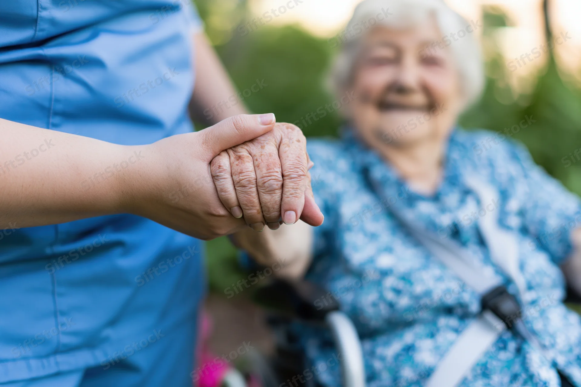 Caregiver holding elderly woman's hand in garden setting