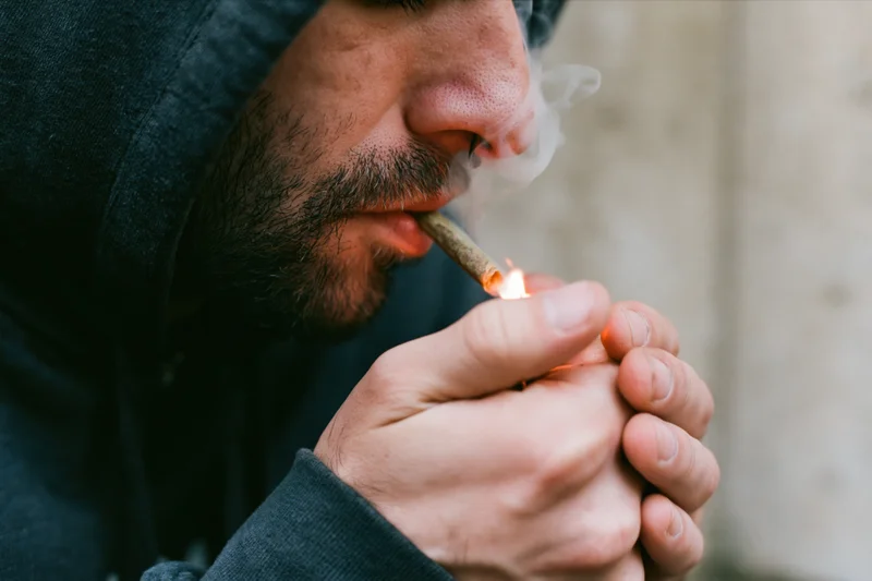 Man lighting a hand-rolled cannabis joint outdoors in a hoodie