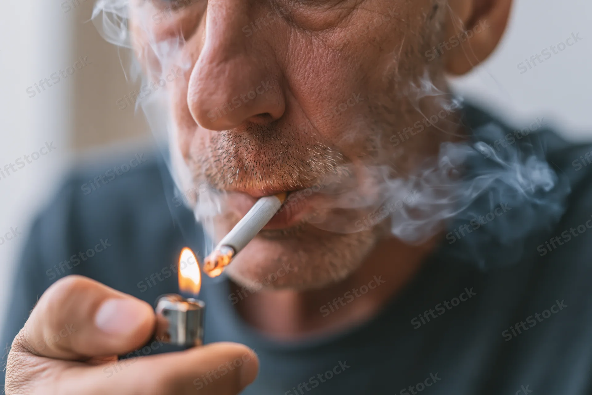 Close-up of a middle-aged man lighting a cigarette with a lighter, smoke curling from his mouth