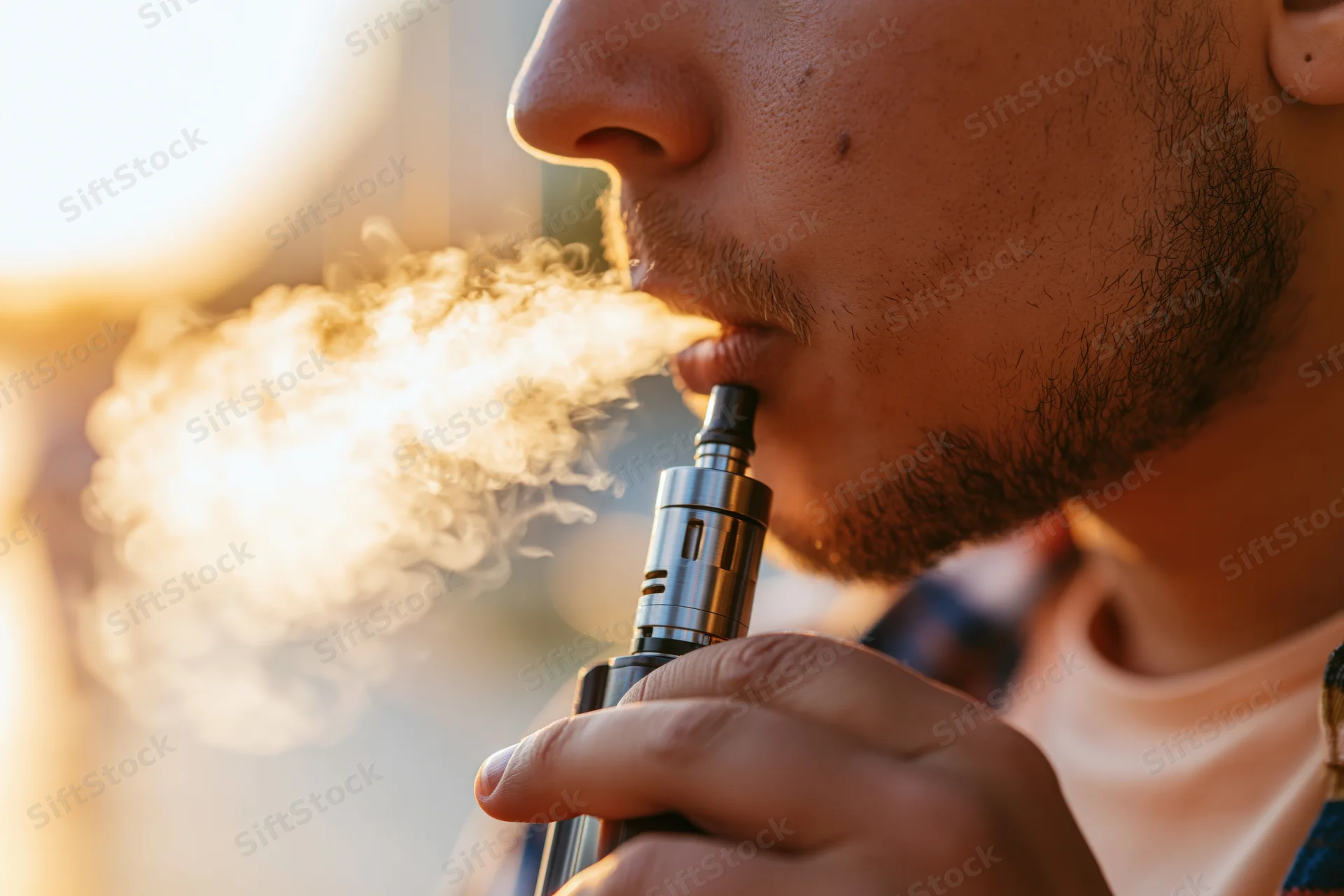 Young man exhaling vapor from e-cigarette in close-up profile view