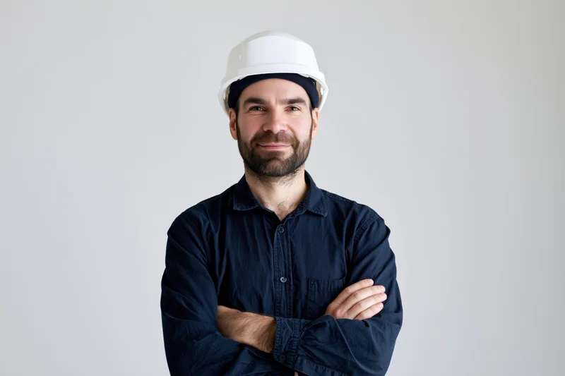 Man in white hard hat and blue shirt with arms crossed standing in studio
