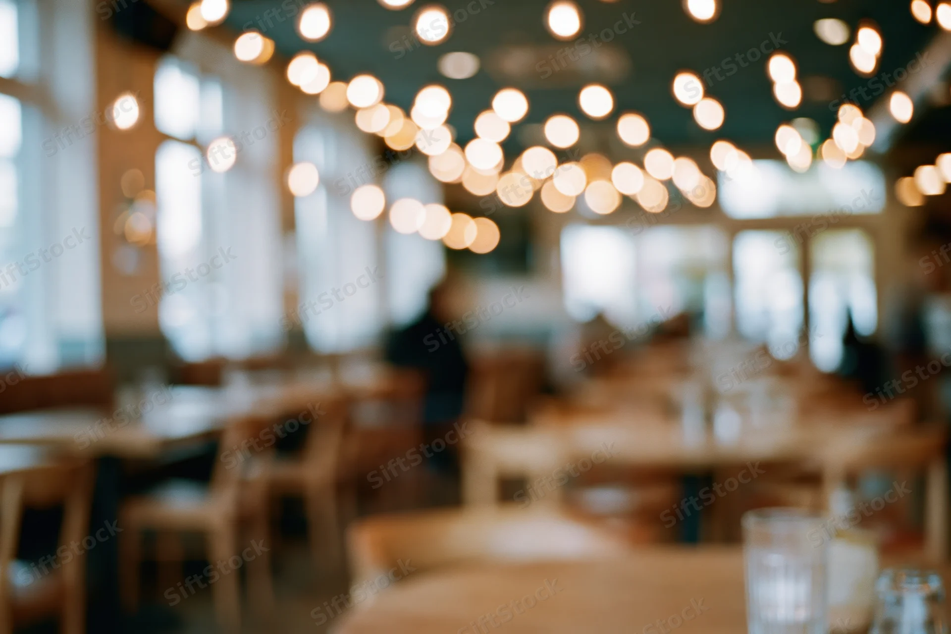 Defocused interior of a cafe with wooden tables and chairs under warm ceiling lights