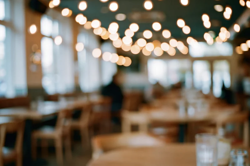 Defocused interior of a cafe with wooden tables and chairs under warm ceiling lights