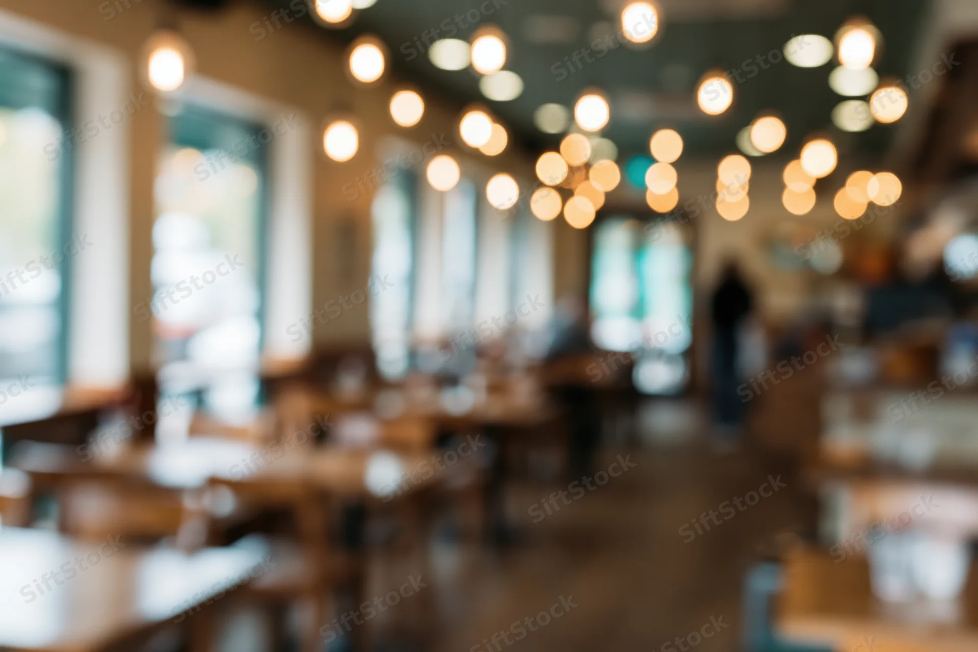 Defocused interior of a casual cafe with wooden tables and chairs under warm pendant lighting