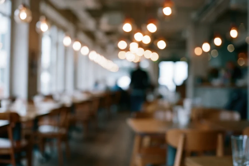 Defocused interior of a casual cafe with wooden tables and chairs under warm pendant lighting