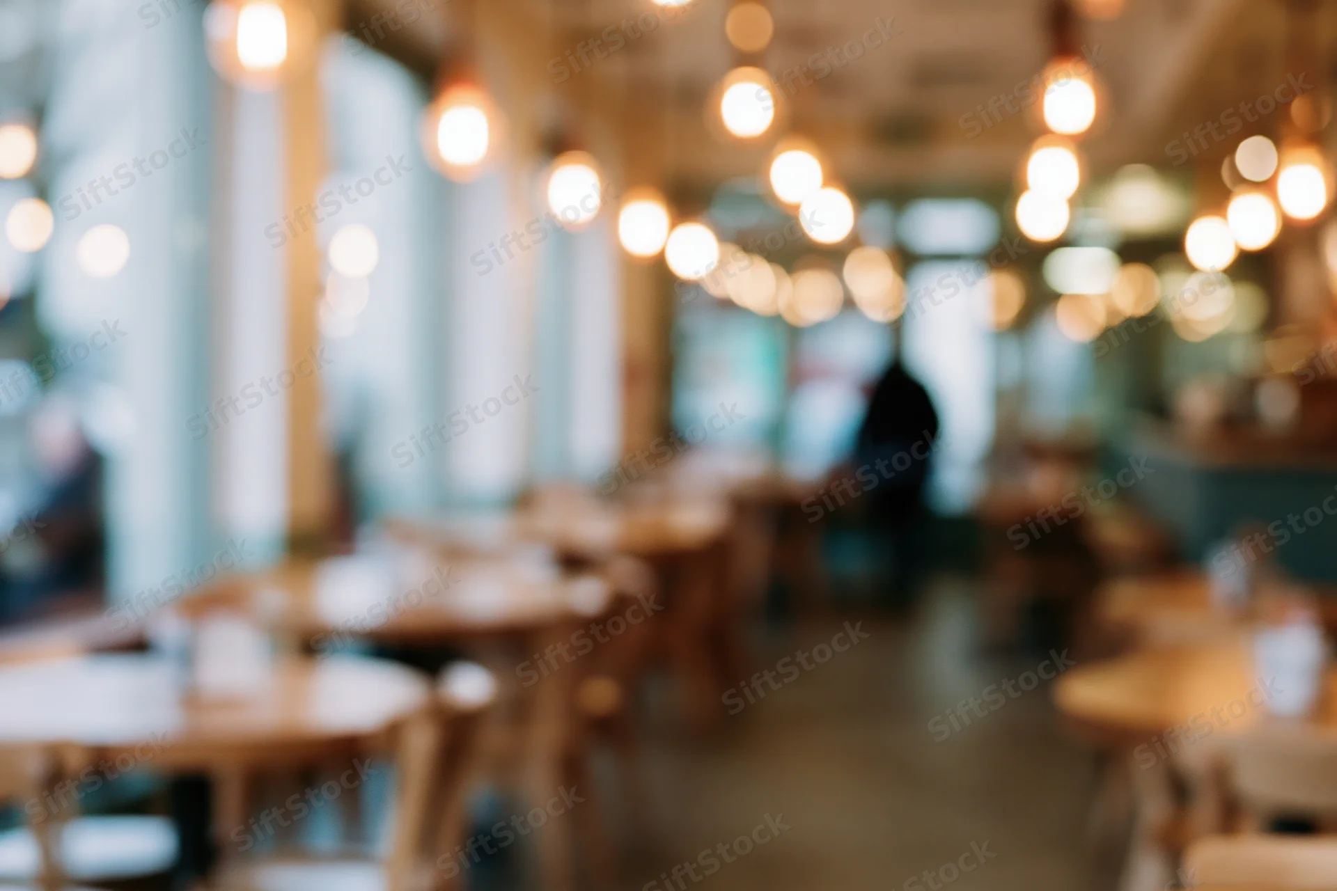 Defocused interior of a casual cafe with wooden tables and chairs under warm pendant lighting