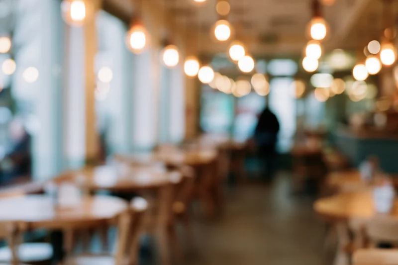 Defocused interior of a casual cafe with wooden tables and chairs under warm pendant lighting