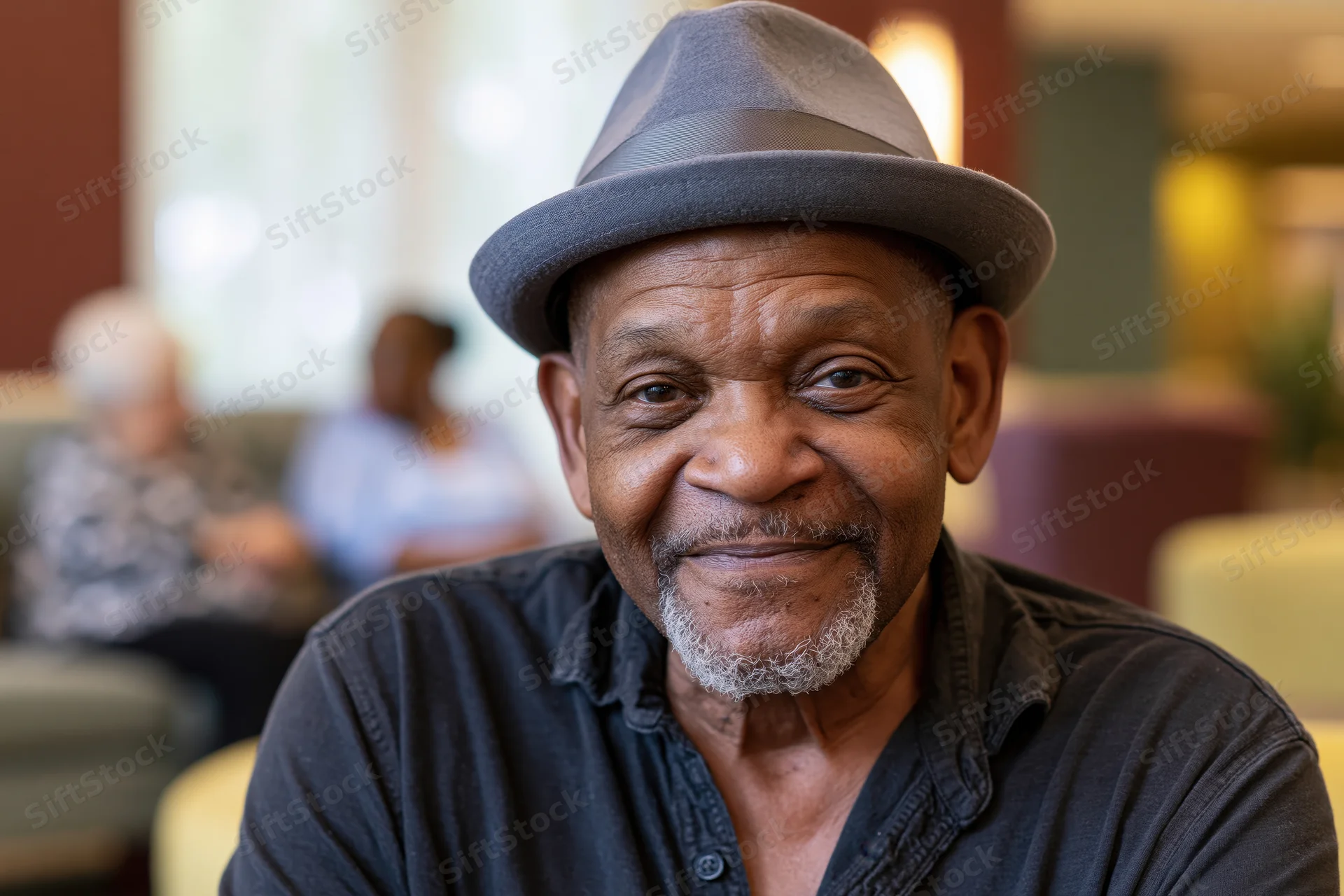 Senior black man smiling softly while wearing a grey fedora hat indoors