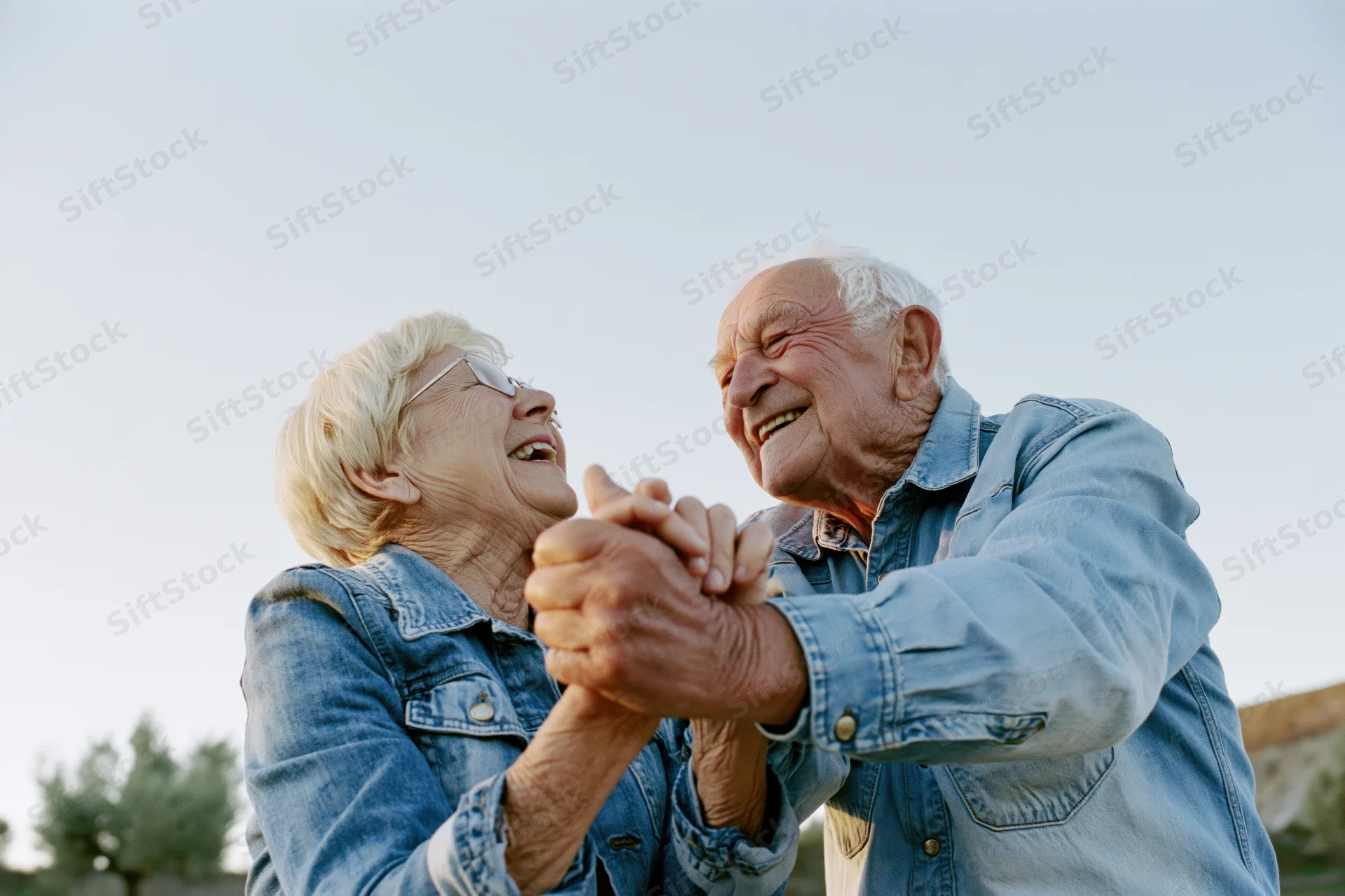 Elderly couple dancing and laughing outdoors holding hands