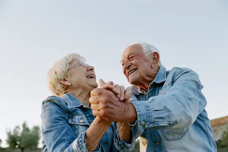 Elderly couple dancing and laughing outdoors holding hands
