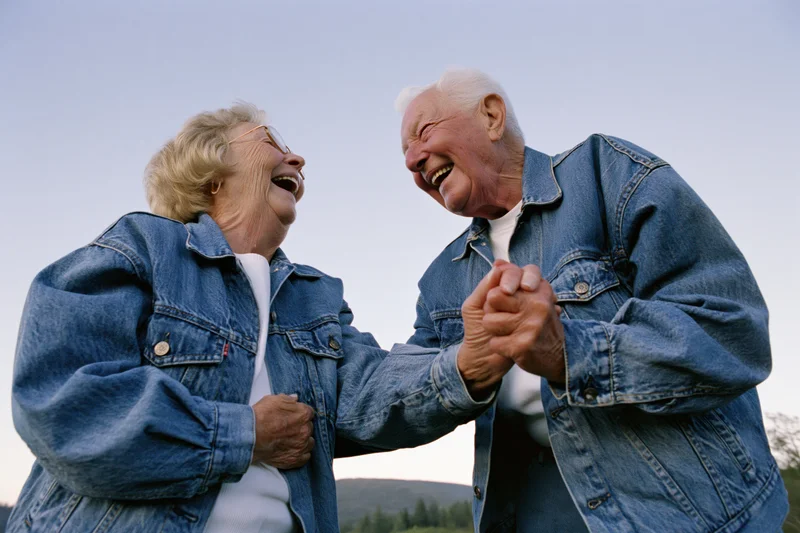 Elderly couple laughing and dancing outdoors holding hands